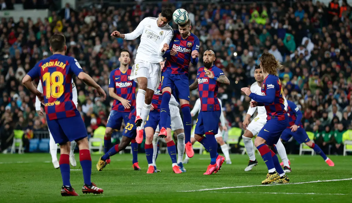 Bek Real Madrid Raphael Varane (kiri tengah) dan pemain Barcelona, Gerard Pique melompat saat berebut bola pada lanjutan pertandingan La Liga di Santiago Bernabeu, Minggu (2/3/2020).  Real Madrid membungkam Barcelona 2-0 dan merebut puncak klasemen dari Barcelona . (AP/Manu Fernandez)