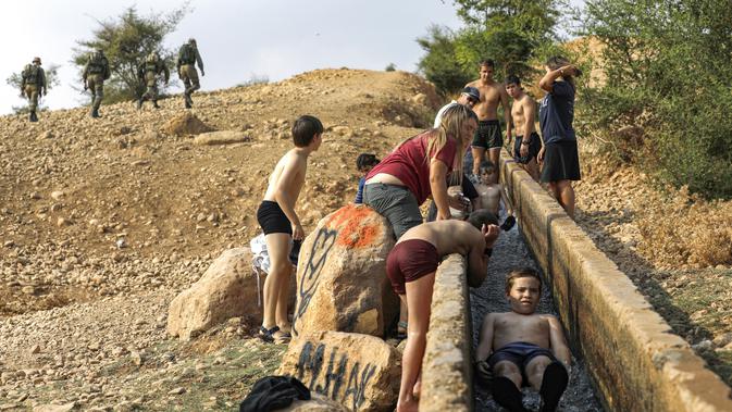Anak-anak Israel bermain air di sebuah kanal kecil di Desa Al-Auja selama perayaan keagamaan Yahudi dalam Festival Sukkot di Tepi Barat (17/10/2019). Festival Yahudi di Sukkot memperingati pengembaraan padang pasir alkitabiah orang Israel setelah eksodus mereka dari Mesir. (AFP Photo/Menahem Kahana)