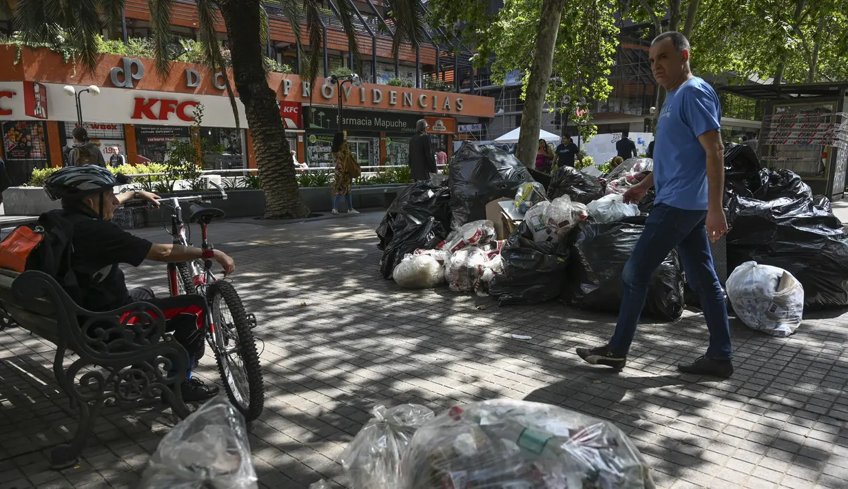 Seorang pria berjalan melewati tumpukan sampah akibat pemogokan petugas sampah di Santiago (14/11/2019). Protes kekerasan meletus di ibukota Chile, Santiago, pada Selasa ketika mata uang negara itu turun ke level terendah dalam sejarah. (AFP/Javier Torres)