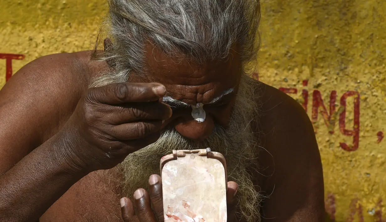 Seorang Sadhu atau orang suci Hindu mengoleskan cat di wajahnya menjelang festival Hindu 'Maha Shivaratri', di dekat kuil Pashupatinath di Kathmandu (9/3/2021). Orang Suci Hindu tidak diizinkan untuk menjual atau membiarkan peziarah mengisap ganja. (AFP/Prakash Mathema)