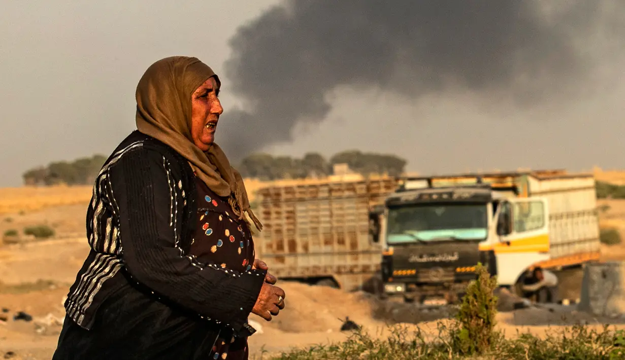 Seorang wanita berjalan saat asap mengepul menyusul pemboman Turki di Kota Ras al-Ain, Provinsi Hasakeh, Suriah, Rabu (9/10/2019). Turki mulai menggelar operasi militer untuk menyasar milisi Kurdi di utara Suriah. (Delil SOULEIMAN/AFP)