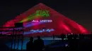 Orang-orang mengambil gambar piramida besar Kheops yang memproyeksikan tulisan "Stay home, all united" di tengah penyebaran pandemi corona Covid-19 di Giza, Mesir, Senin (30/3/2020). Piramida itu menampilkan pesan dalam bahasa Arab dan Inggris dalam cahaya berwana biru dan hijau (Khaled DESOUKI/AFP)