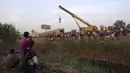 Sebuah crane digunakan untuk mengangkat bagian dari kereta penumpang yang tergelincir dekat Banha, Provinsi Qalyubia, Mesir, Minggu (18/4/2021). Sebanyak 60 ambulans dikerahkan ke lokasi untuk membawa korban ke rumah sakit-rumah sakit terdekat. (AP Photo/Fadel Dawood)