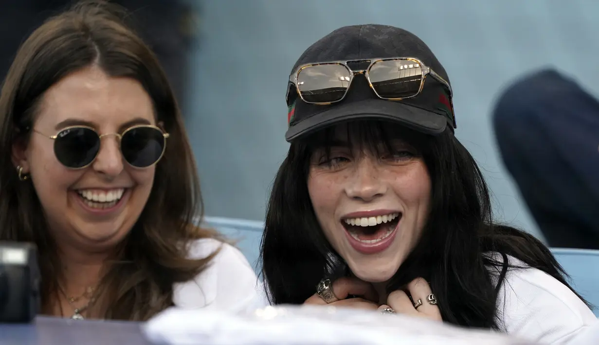 Penyanyi Billie Eilish (kanan) tersenyum di tribun sebelum pertandingan bisbol antara Los Angeles Dodgers dan San Francisco Giants di Los Angeles, Amerika Serikat, 21 Juli 2022. Billie Eilish tampil kasual dengan T-shirt hitam longgar, topi bisbol putih, dan kacamata hitam. (AP Photo/Marcio Jose Sanchez)