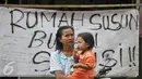 Seorang ibu menggendong anaknya berdiri di depan spanduk penolakan penggusuran kawasan Bukit Duri, Jakarta, Rabu (28/9). Pemprov DKI akhirnya melakukan penertiban pemukiman di Bukit Duri terkait revitalisasi sungai Ciliwung. (Liputan6.com/Yoppy Renato)