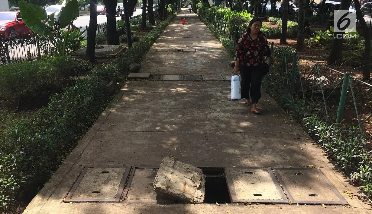 Pejalan kaki melintasi trotoar yang rusak dan berlubang di Jalan Kyai Tapa, Jakarta, Kamis (24/1). Banyaknya lubang akibat kerusakan penutup saluran air tersebut membahayakan pejalan kaki. (Liputan6.com/Immanuel Antonius)