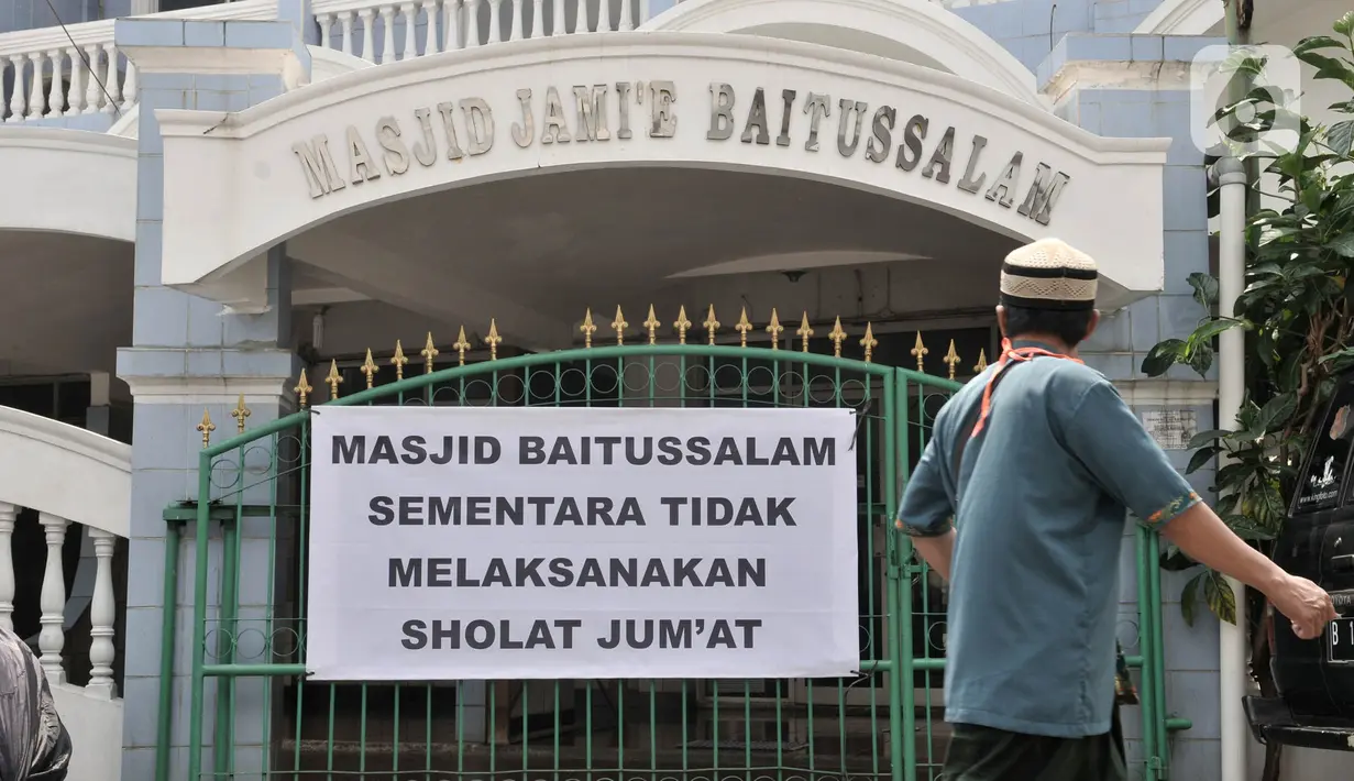 Jemaah melintasi spanduk pemberitahuan yang dipasang oleh petugas di Masjid Jami'e Baitussalam, Cipinang, Jakarta, Jumat (10/4/2020). (merdeka.com/Iqbal S. Nugroho)