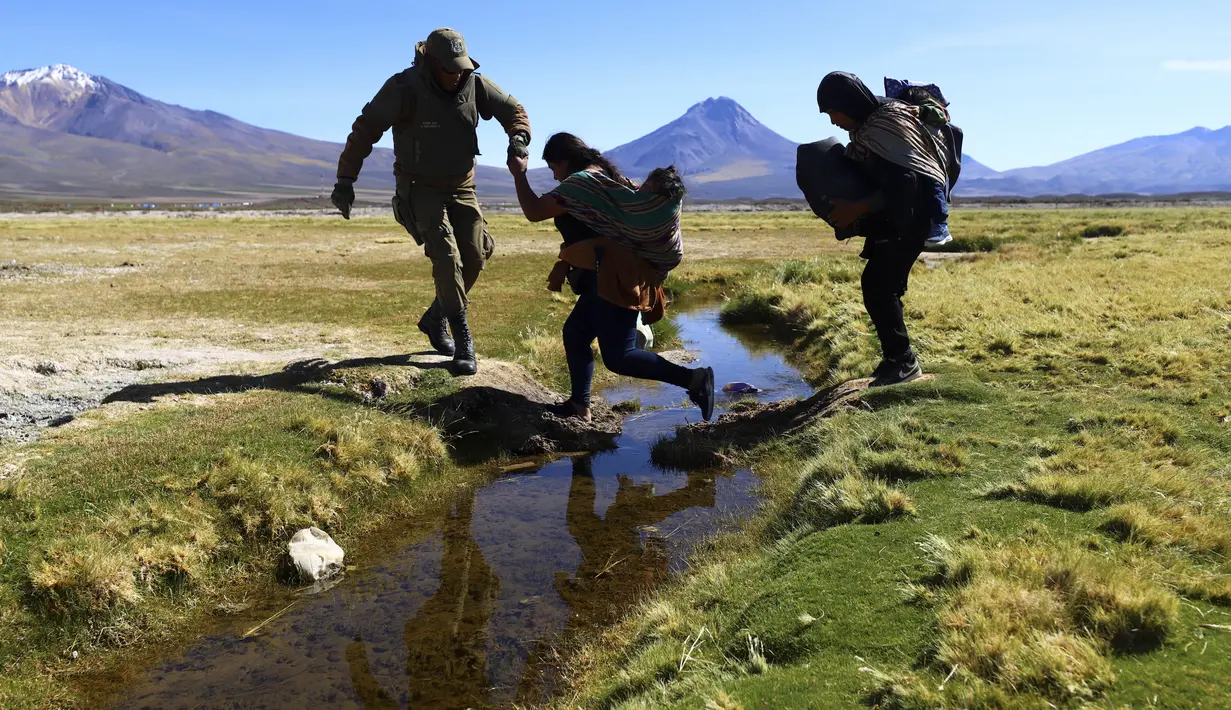 Seorang tentara Chili membantu seorang migran menyeberangi kanal air sebelum membawa mereka ke tempat penampungan di mana polisi mendaftarkan mereka, dekat Colchane, Chili, Rabu, 1 Maret 2023. Langkah tersebut adalah yang terbaru oleh pemerintah paling kiri Chile dalam 50 tahun untuk mencoba mengembalikan kemerosotan popularitasnya setelah satu tahun menjabat. (AP Photo/Ignacio Munoz)