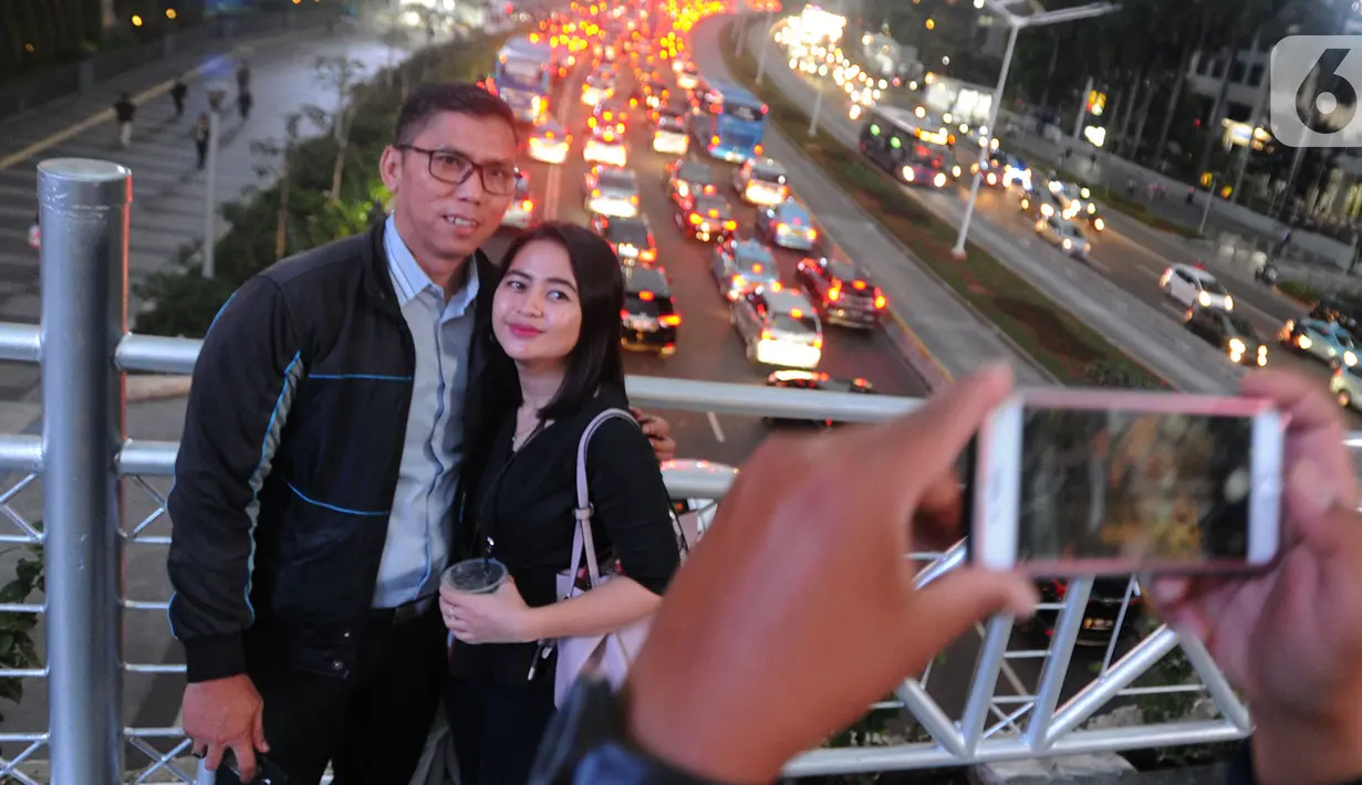 Warga berfoto di jembatan penyeberangan orang (JPO) yang tidak beratap di jalan Sudirman, Jakarta, Rabu (6/11/2019). Pemprov DKI mengklaim mayoritas masyarakat Jakarta setuju dengan konsep JPO terbuka dan tanpa atap yang kini dibangun di Sudirman. (merdeka.com/Arie Basuki)