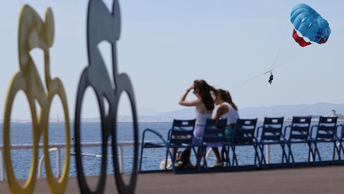 Wisatawan menikmati suasana pantai di dekat ornamen Tour De France 2020 di kota Nice, French Riviera, Rabu (26/8/2020). Ajang balap sepeda lintas kota di Prancis kali ini akan dimulai dari kota Nice pada 29 Agustus hingga 20 September di tengah kehawatiran COVID-19. (Kenzo Tribouillard/AFP)
