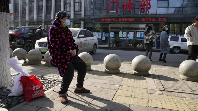 Seorang warga yang mengenakan masker duduk di luar pintu masuk klinik Rumah Sakit Provinsi Hubei, di mana tim peneliti WHO tiba pada kunjungan lapangan pertamanya untuk mencari petunjuk tentang asal-usul pandemi COVID-19. (AP / Ng Han Guan)