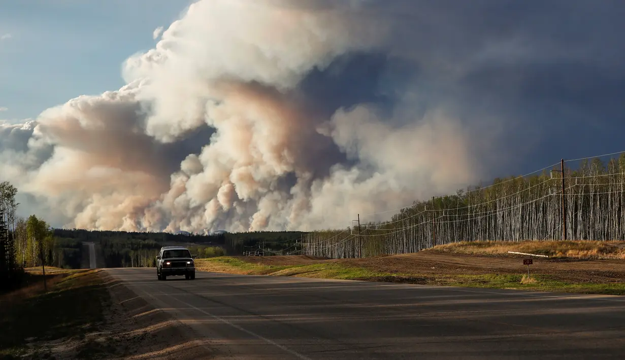 Sebuah mobil berjalan melintas berada tak jauh dari kepulan asap yang membakar hutan di wilayah Fort McMurray, Alberta, Kanda, 4 Mei 2016. Sekitar 80 ribu warga Kanada terpaksa dievakuasi Akibat kebakaran dahsyat ini. (REUTERS / Mark Blinch)