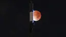 Bulan terlihat saat gerhana bulan di belakang One World Trade Center di New York , Jumat dini hari (19/11/2021). Gerhana bulan yang diamati pada tanggal 18 dan 19 November di berbagai wilayah dunia ini merupakan gerhana parsial yang terpanjang pada abad ini. (Yuki IWAMURA / AFP)