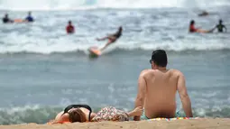 Dua turis berjemur di pantai Kuta di pulau pariwisata Indonesia di Bali (4/1). Sebelum menjadi objek wisata, Kuta merupakan sebuah pelabuhan dagang tempat produk lokal diperdagangkan kepada pembeli dari luar Bali. (AFP Photo/Sony Tunbelaka)