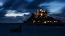Kastil Mont Saint-Michel terlihat saat malam hari di Normandia, Prancis barat laut (31/8/2019). Mont Saint-Michel yang berjuluk ‘Wonder of the West’ bertengger di pulau berbatu di tengah gumuk pasir antara Normandia dan Brittany. (AFP Photo/Joel Saget)
