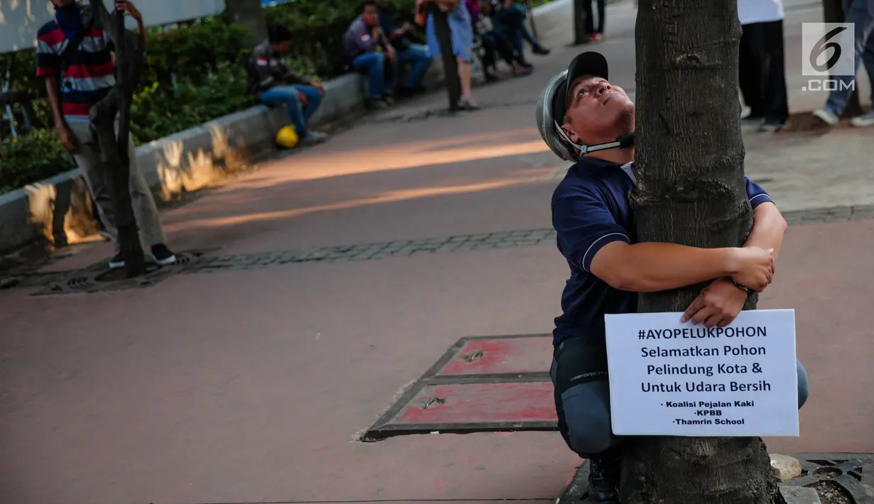 Seorang pria memeluk pohon sambil membentangkan poster saat menggelar aksi #ayopelukpohonini di Jalan Sudirman, Jakarta, Jumat (22/9). (Liputan6.com/Faizal Fanani)