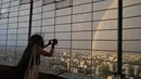Seorang wanita mengambil foto pelangi ganda melalui pagar di Central Television Tower di Beijing (26/8/2021). Keindahan pelangi ganda dimanfaatkan warga Beijing untuk diabadikan lewat foto dan berfoto dengan latar pelangi itu. (AFP/Jade Gao)