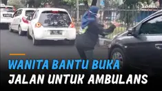 Seorang wanita turun dari kendaraan dan menuntun ambulans menembus kemacetan.