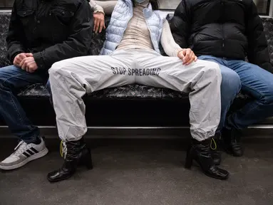Elena Buscaino berpose dengan Riot Pants di antara dua pria di kereta bawah tanah di Berlin, 5 Februari 2021. Aktivis feminis Elena Buscaino dan Mina Bonakdar sedang dalam misi menghentikan kebiasaan penumpang pria melebarkan kaki saat duduk sehingga memakan dua kursi kereta. (STEFANIE LOOS/AFP)