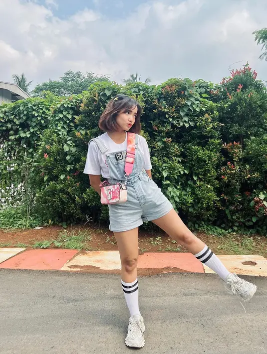 Fuji tampil manis memadukan kaus putih polos lengan pendek dengan overall jeans pendek. Ia menambahkan kaus kaki tinggi dan sneakers putih, serta sling bag pink. [Foto: Instagram/fuji_an]