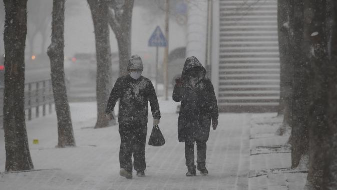 Orang-orang memakai masker sebagai pencegahan virus corona berjalan di salju di Goyang, Korea Selatan, Kamis (28/1/2021). Administrasi Meteorologi Korea (KMA) memperkirakan sebagian besar negara itu akan melihat hujan atau salju pada siang hari yang dimulai dengan wilayah barat. (AP/Lee Jin-man)