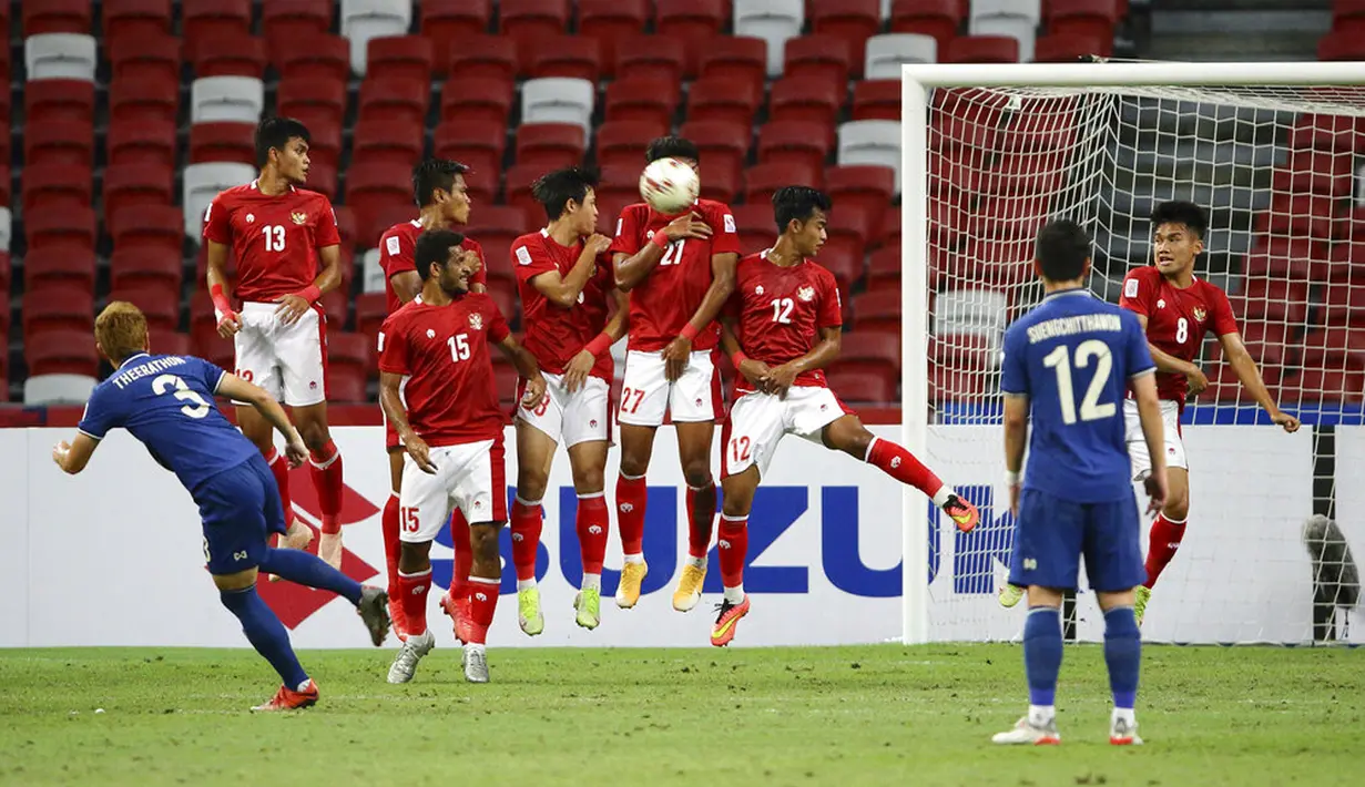 Pemain Indonesia melompat untuk menghalau tendangan bebas pemain Thailand Theerathon Bunmathan (kiri) pada pertandingan sepak bola leg kedua final Piala AFF 2020 di National Stadium, Singapura, Sabtu (1/1/2022). Pertandingan berakhir dengan skor 2-2. (AP Photo/Suhaimi Abdullah)
