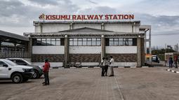 Penduduk setempat berdiri di depan stasiun kereta Kisumu, pada Jumat (17/12/2021). Kereta api Kenya melanjutkan layanan komuter antara Nairobi dan Kisumu setelah tidak beroperasi selama lebih dari 10 tahun. (Brian ONGORO/AFP)