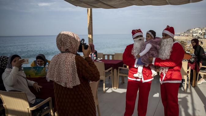 Pramusaji Palestina berpakaian Sinterklas menggendong seorang anak untuk berfoto di sebuah restoran di pantai di Kota Gaza, Minggu (13/12/2020). REstoran tersebut didandani dengan tema Natal, pelayanannya pun berpakaian seperti Sinterklas. (AP Photo/Khalil Hamra)