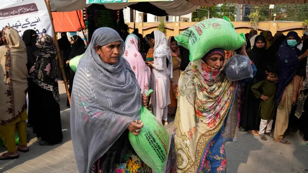 Perempuan dengan sekarung tepung terigu gratis di tempat distribusi sembako Ramadhan di Lahore, Pakistan [File: KM Chaudary/AP]