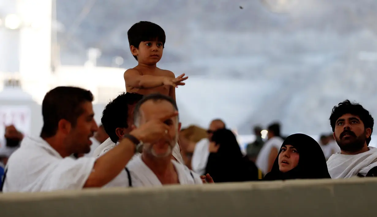 Jemaah haji melempar jumrah sambil menggendong anak sebagai simbol mengusir setan saat ibadah haji di Mina, Arab Saudi (12/09). (REUTERS/Ahmed Jadallah)