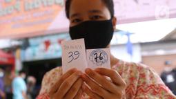 Warga menunjukkan nomor antrean membeli minyak goreng dan daging kerbau seusai vaksincovid-19 di kawasan Tanah Tinggi, Kota Tangerang, Jumat (4/3/2022). Pemkot Tangerang mengadakan operasi pasar minyak dan daging murah bagi warga yang melaksanakan vaksinasi di lokasi. (Liputan6.com/Angga Yuniar)