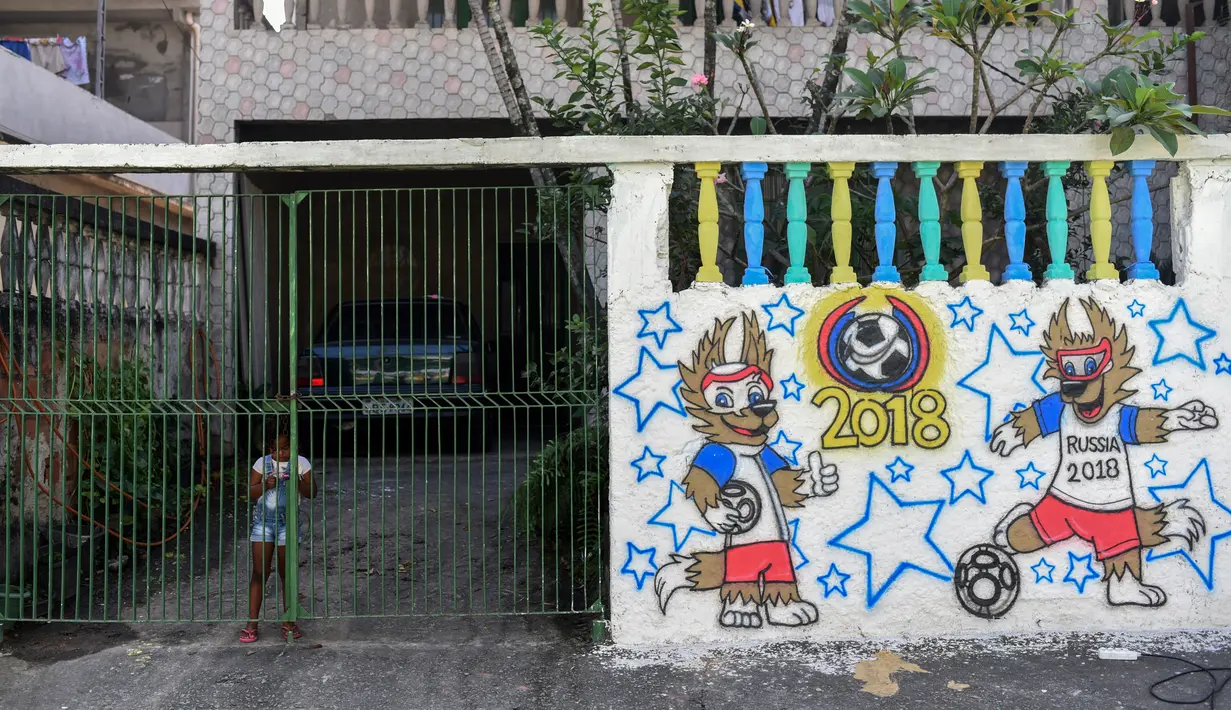 Seorang gadis berdiri di belakang gerbang pada sebuah mural Piala Dunia 2018 di dinding jalanan Camboata, Rio de Janeiro, Brasil, Kamis (31/6). (Fabio TEIXEIRA/AFP)