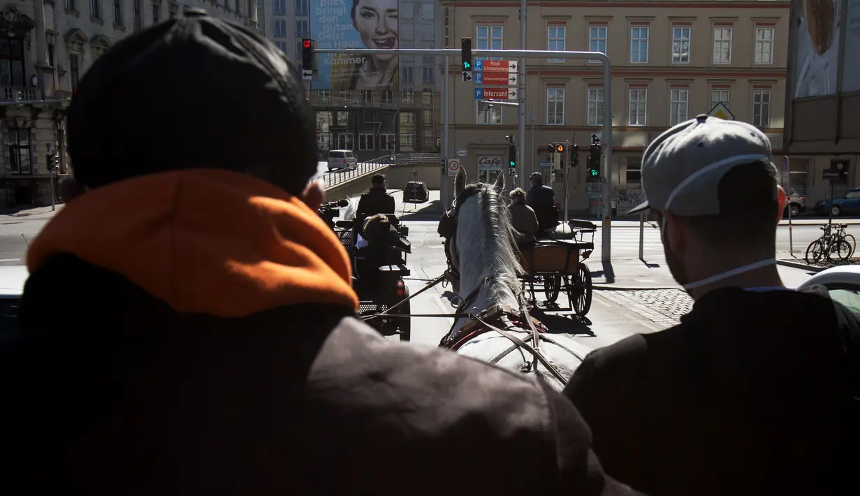 Pengemudi mengendarai kereta kuda di sebuah jalan di distrik ke-3 di Wina, Austria pada 8 April 2020. Kereta yang disebut Fiaker yang biasanya mengangkut turis semenjak pandemi Corona beralih fungsi menjadi pengantar makanan untuk lanjut usia di daerah tersebut. (ALEX HALADA/AFP)