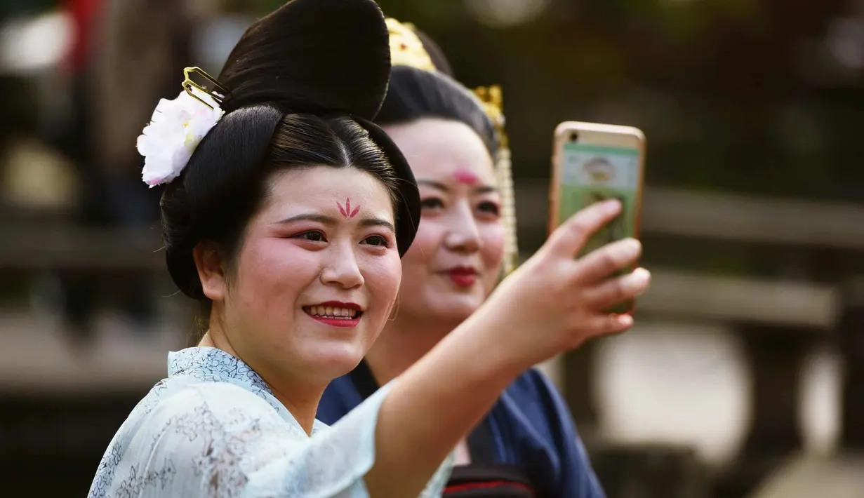 Dua wanita berselfie mengenakan kostum Dinasti Tang saat mengunjungi Danau Barat di Hangzhou di provinsi Zhejiang timur China (31/3). Kostum Dinasti Tang memiliki Struktur alami, anggun dan elegan, dan aksesoris yang indah. (AFP Photo/China Out)