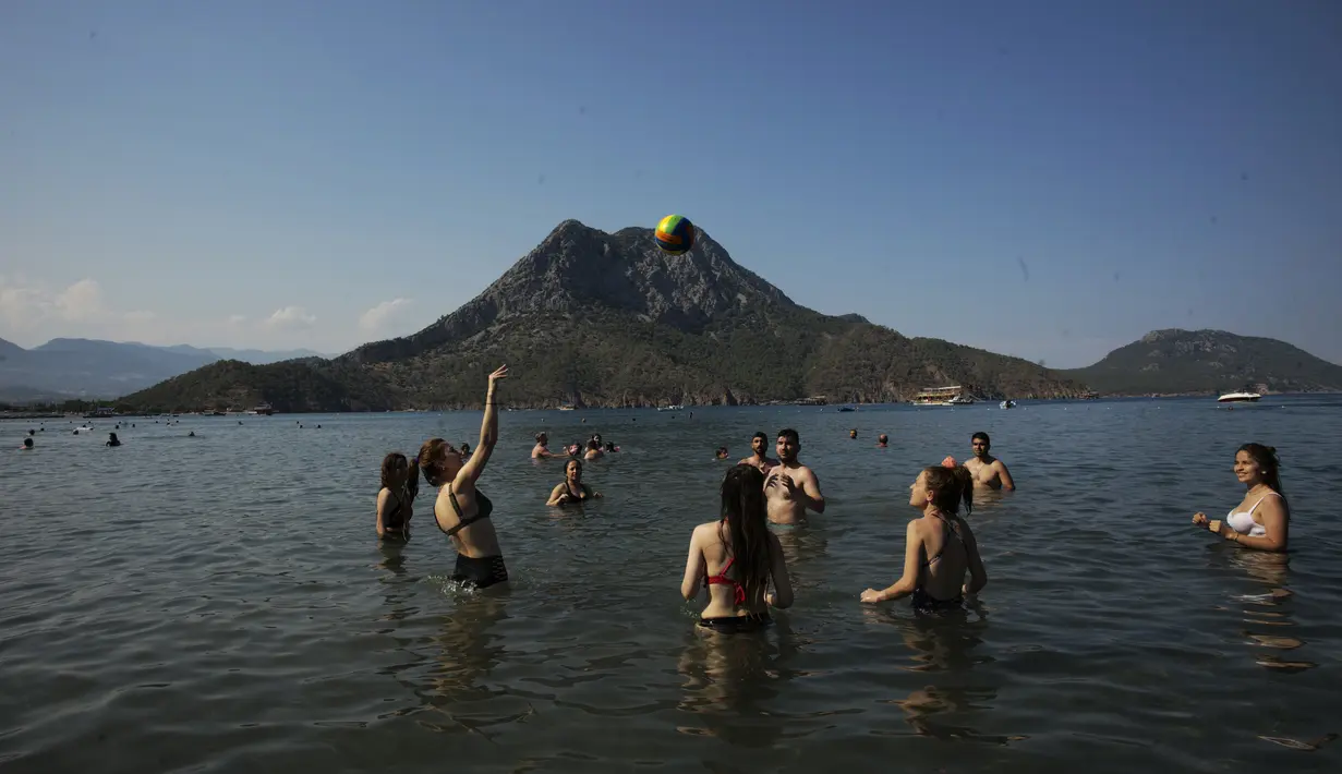 Orang-orang bermain bola voli saat menikmati cuaca cerah, laut dan matahari, sehari sebelum jam malam hari Minggu di Adrasan, 100 kilometer barat Antalya, di Mediterania Turki, Sabtu (19/6/2021).  (AP Photo/Burhan Ozbilici)