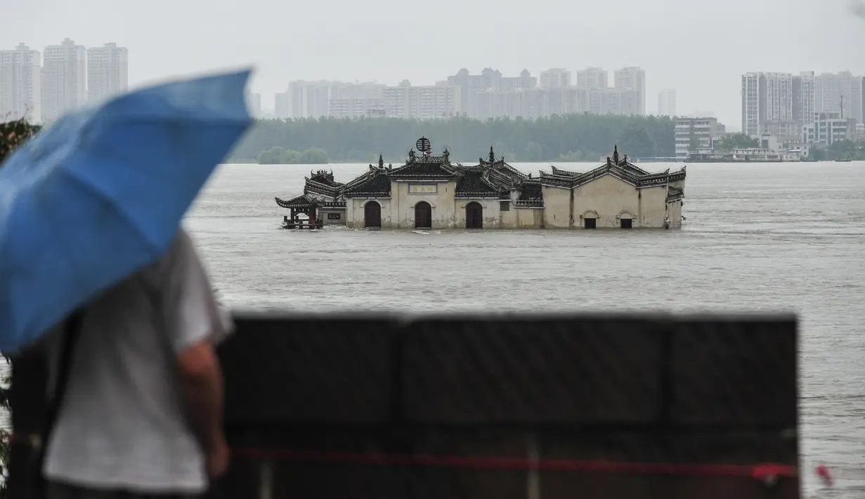 Warga memandangi kuil Guanyinge berumur 700 tahun yang dibangun di atas batu, terendam banjir akibat meluapnya sungai Yangtze di Wuhan, provinsi Hubei pada 19 Juli 2020. Hujan lebat sejak bulan Juni telah menyebabkan sedikitnya 141 orang tewas dan memaksa hampir 15 juta orang dievakuasi. (STR/AFP)
