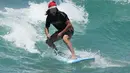 Tony O'Connor, asal Manchester, Inggris, naik papan selancar sambil mengenakan topi Santa saat merayakan Natal di Bondi Beach di Sydney, Sabtu (25/12/2021). (AP Photo/Rick Rycroft)