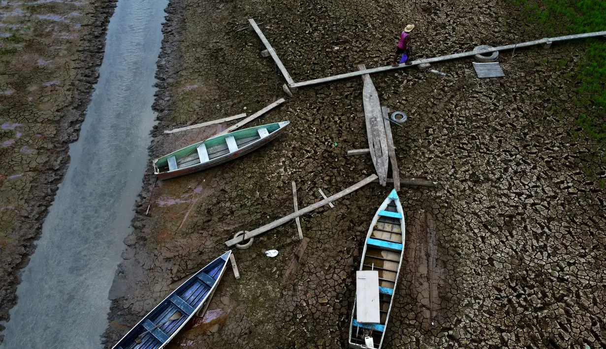 Seorang warga berjalan di samping perahu di hamparan Sungai Solimoes yang kering, akibat suhu tinggi yang melanda wilayah kota Manaquiri, di daerah pedesaan negara bagian Amazonas, Brasil, Sabtu, 21 Oktober 2023. (AP Photo/Edmar Barros)