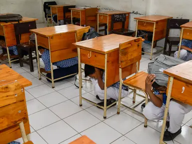 Sejumlah siswa berlindung di bawah meja saat simulasi bencana gempa dan tsunami di sebuah sekolah di Banda Aceh, Aceh, Rabu (9/10/2019). Para siswa dibekali wawasan tanggap darurat bencana dan pemberian pertolongan pertama pada korban gempa. (Photo by CHAIDEER MAHYUDDIN / AFP)