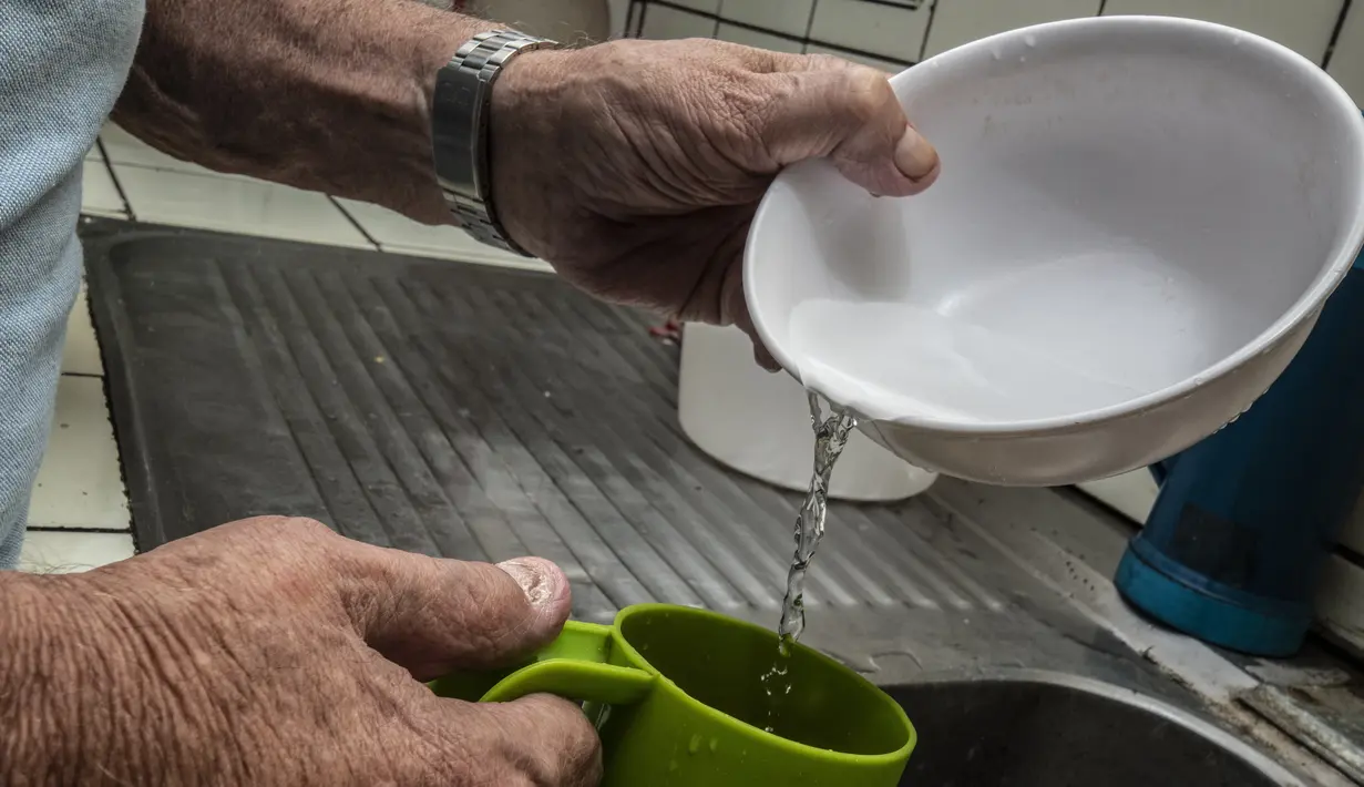 Seorang pria mencuci piring dengan air yang dikumpulkan karena penjatahan air di San Jose pada 12 Juli 2023. (Ezequiel BECERRA / AFP)