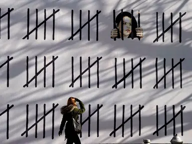 Seorang wanita pejalan kaki melihat mural baru karya seniman misterius Inggris, Banksy di wilayah Manhattan, New York (15/3). Mural ini memprotes penahanan seniman Turki Zehra Dogan karena lukisannya. (AFP Photo/Timothy A. Kliit)