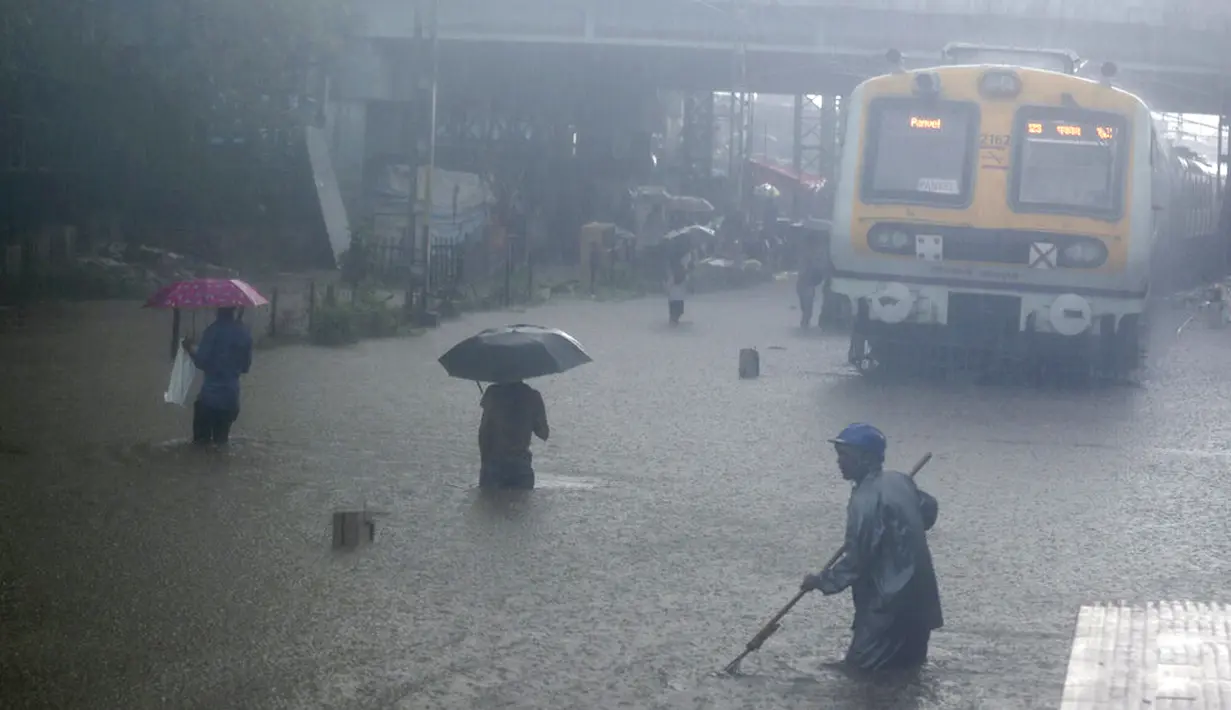 Warga melintasi rel kereta api yang terendam banjir saat hujan lebat di Mumbai, India, Rabu (9/6/2021). Mumbai terendam banjir usai diguyur hujan lebat. (AP Photo/Rafiq Maqbool)