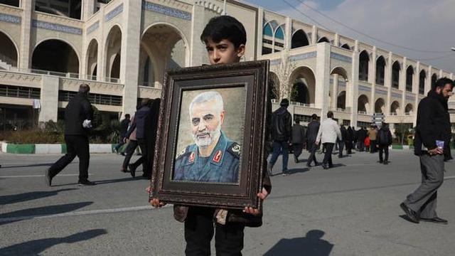Seorang bocah laki-laki memegang foto Qasem Soleimani dalam acara pemakamannya.