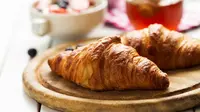Dua buah croissant di atas sebuah piring berbahan kayu (Foto Dok: Freepik/valeria_aksakova).