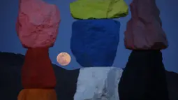 Supermoon terlihat dari celah instalasi seni Seven Magic Mountains karya seniman Ugo Rondinone di Las Vegas, Amerika Serikat, Selasa (7/4/2020). Seven Magic Mountains terdiri dari tujuh buah bangunan yang disusun dari batuan besar warna-warni. (AP Photo/John Locher)