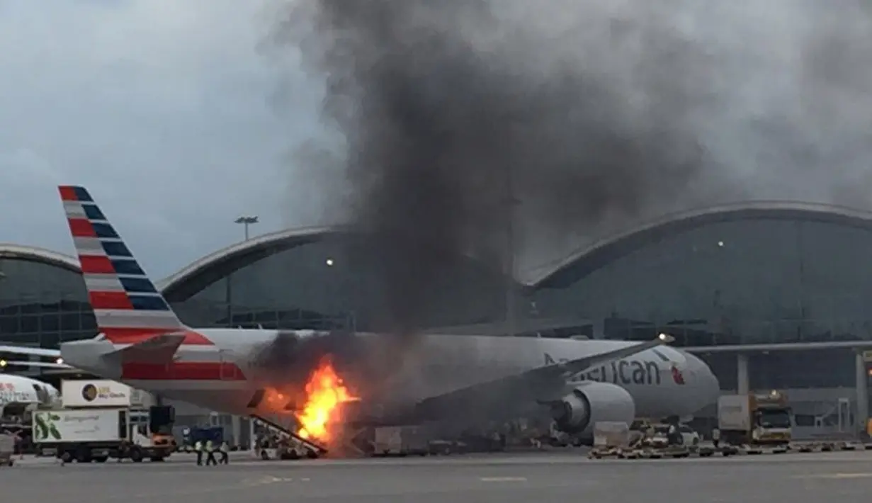 Sebuah kebakaran terjadi di landasan pacu Bandara Internasional Hong Kong, Senin (9/10). Kobaran api dan kepulan asap hitam terlihat di dekat perut badan pesawat milik maskapai American Airlines. (U87 via AP)