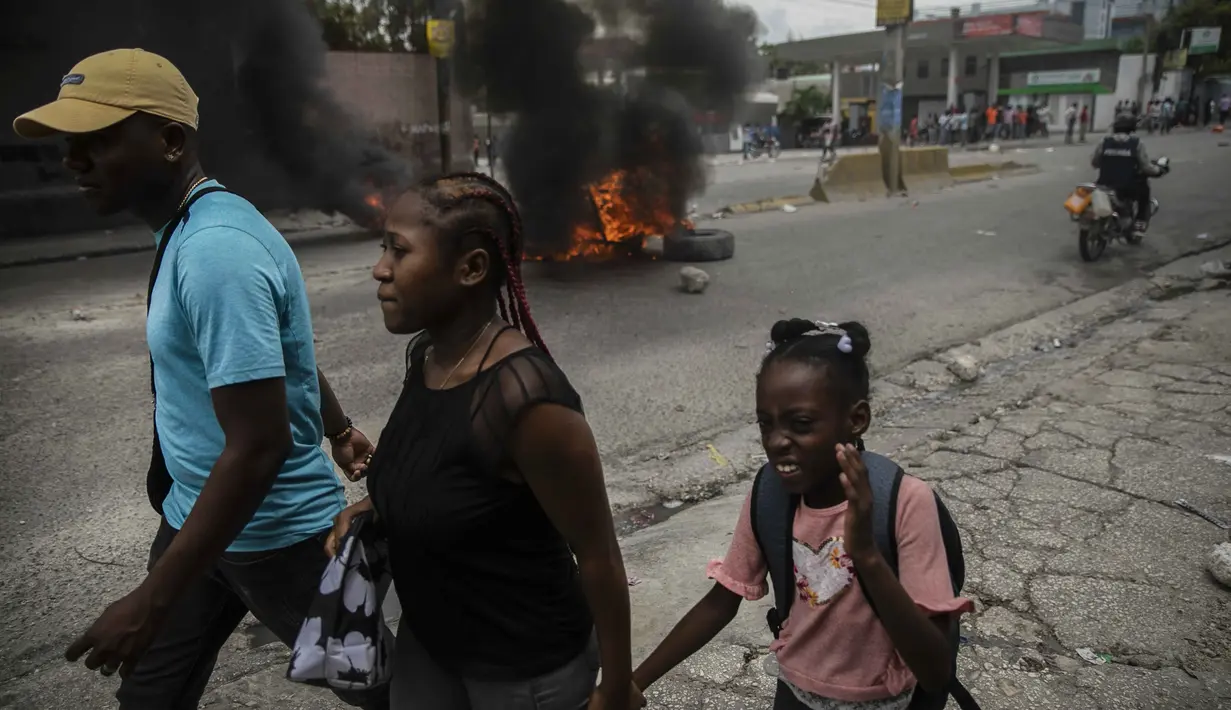 Orang-orang berjalan di sekitar ban yang dibakar oleh pengunjuk rasa untuk menuntut Perdana Menteri Haiti Ariel Henry mundur dan menyerukan kualitas hidup yang lebih baik, di Port-au-Prince, Haiti, Senin (29/8/2022). (AP Photo/Odelyn Joseph)