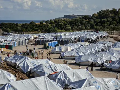 Para migran mengisi air sementara yang lain membersihkan barang-barang mereka setelah hujan badai di kamp pengungsi Kara Tepe, di timur laut pulau Lesbos, Yunani (14/10/2020). (AP Photo/Panagiotis Balaskas)