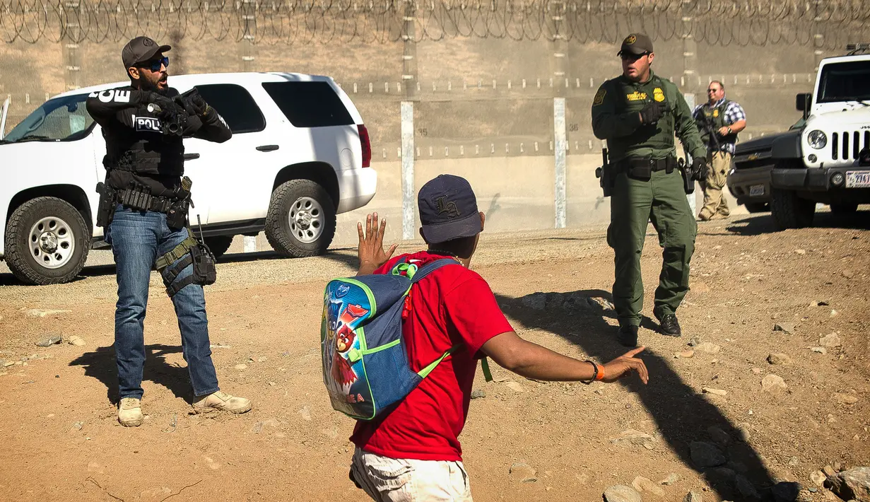 Seorang migran Amerika Tengah dihentikan agen AS yang memerintahkannya untuk kembali ke sisi perbatasan Meksiko, setelah sekelompok migran berhasil melewati polisi Meksiko di persimpangan Chaparral di Tijuana, Meksiko, (25/11). (AP Photo/Pedro Acosta)