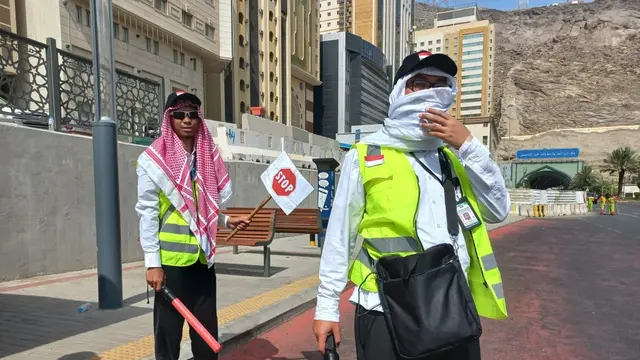 Dua petugas haji dari Indonesia tengah bersiap membantu para jemaah menyeberangi jalan.